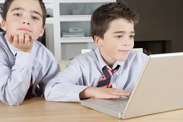 Due fratelli gemelli identici che condividono un computer portatile per fare i compiti — Foto Stock