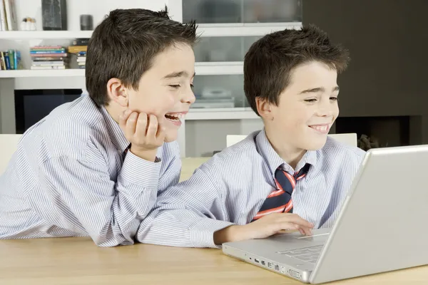 Deux frères jumeaux partageant un ordinateur portable à la maison, riant . — Photo