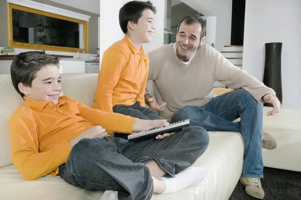 Vater und eineiige Zwillingssöhne fernsehen zu Hause im Wohnzimmer. — Stockfoto