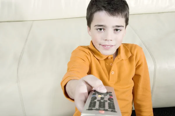 Jeune garçon utilisant une télécommande de télévision tout en regardant la télévision à la maison . — Photo