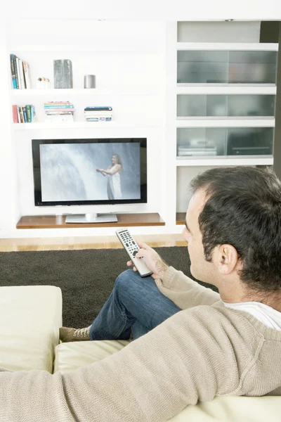 Homem profissional usando um controle remoto de TV para mudar de canais na televisão em casa . — Fotografia de Stock