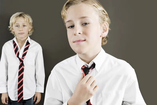 Dos escolares vistiendo uniforme con uno de ellos apretando su corbata . — Foto de Stock