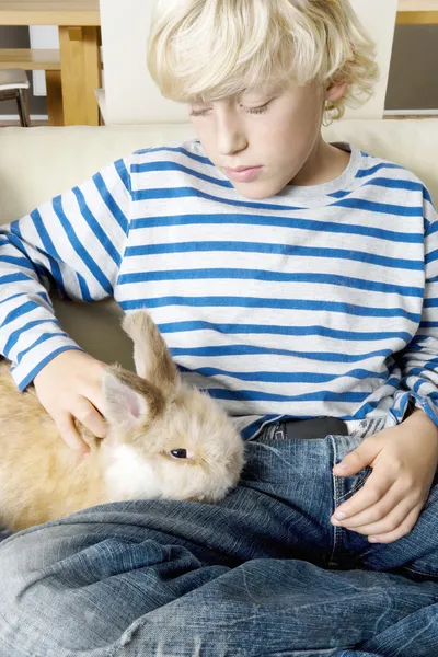 Jonge jongen streelde zijn huisdier konijn thuis. — Stockfoto