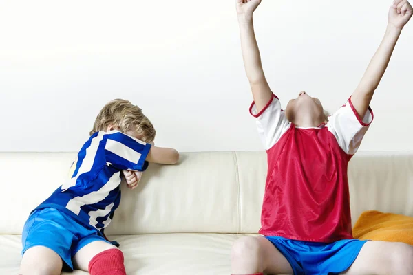 Twee kinderen ondersteunende verschillende teams voetbal kijken en thuis vieren. — Stockfoto