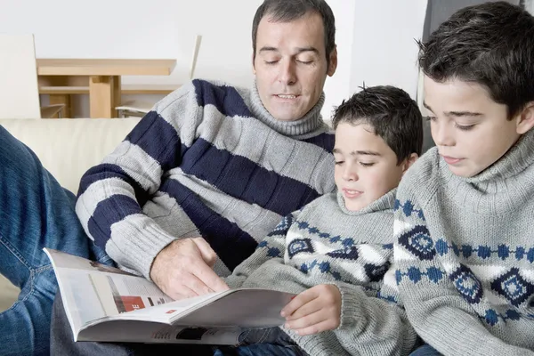 Dad and identical twin sons reading a magazine at home together. — Stock Photo, Image