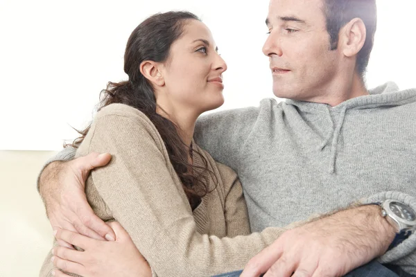 Romantic moment of a hispanic couple sitting down on a while leather sofa at home. — Stock Photo, Image