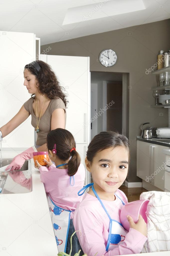 Young mum and daughter washing up and drying dishes in a home kitchen.