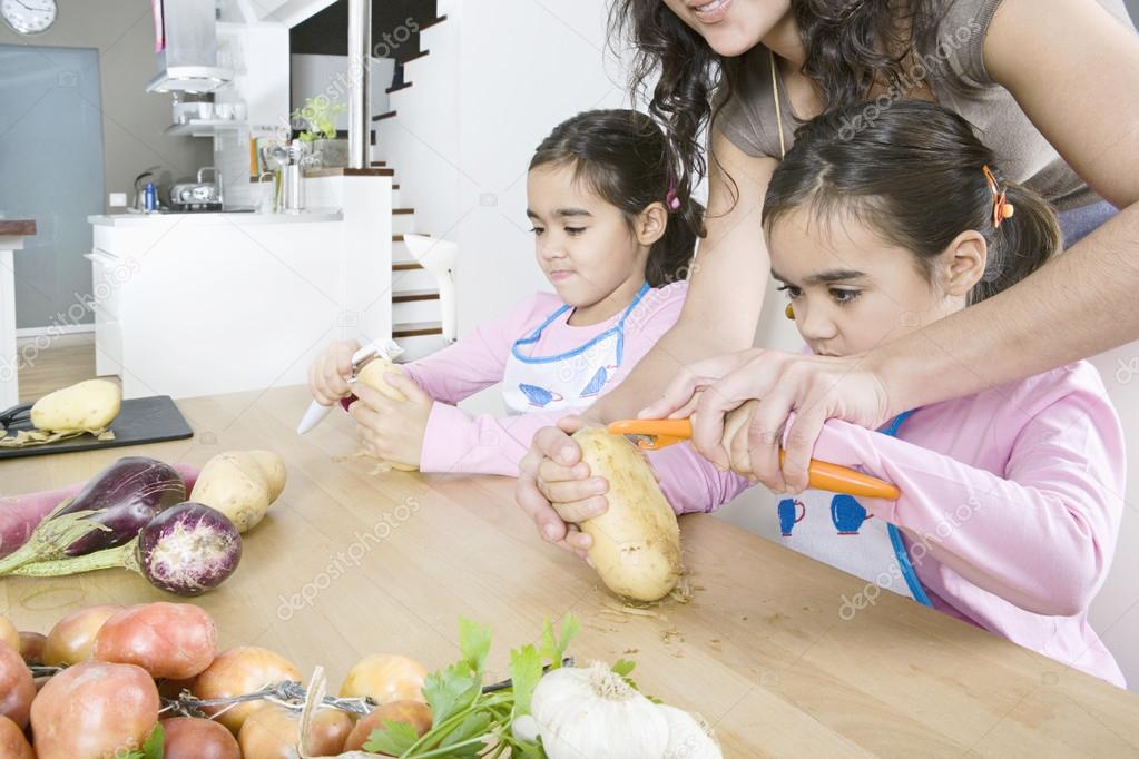 Young mum teaching twin daughters how to peel potatoes.
