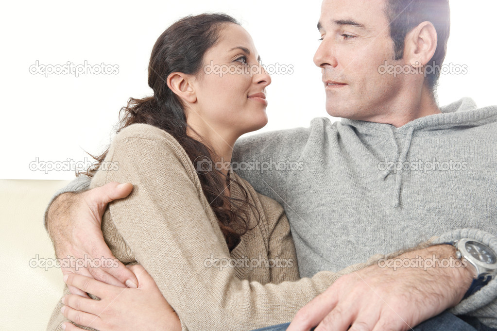 Romantic moment of a hispanic couple sitting down on a while leather sofa at home.