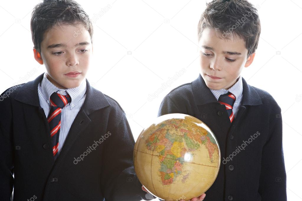 Two identical twin brothers holding a globe map while standing by a window and wearing their school uniform.