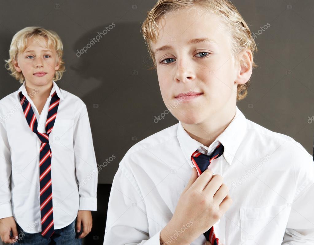 Two brothers getting ready for school at home, wearing uniform shirts and tightening a tie.