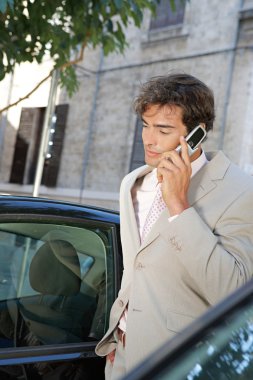 şehir içinde araba tarafından duran bir telefon görüşmesi yapmak için bir cep telefonu kullanarak iş adamı.