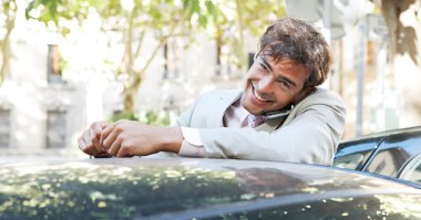 bir cep telefonu kullanarak ve sohbet ederken bir araba şehir içinde yaslanmış çekici işadamı.