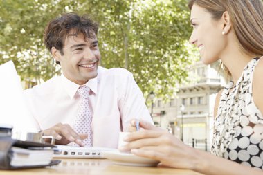 Two business having a meeting in an outdoors cafeteria in the city, smiling. clipart