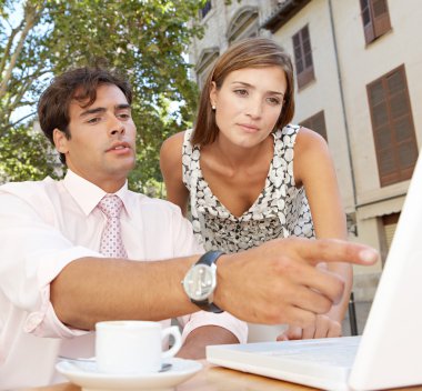 Business colleagues looking at a laptop screen while having a meeting in a coffee shop terrace clipart
