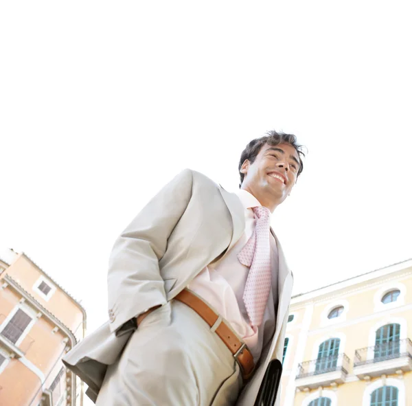 Vista bassa di un giovane uomo d'affari che cammina con una cartella di lavoro in una classica piazza degli edifici per uffici con il cielo dietro di lui . — Foto Stock