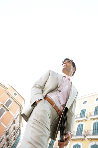 Låg syn på en ung affärsman går förbi med en arbetsmapp i en klassisk kontorsbyggnader kvadrat med himlen bakom honom. — Stockfoto