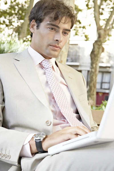 Close up retrato de um homem de negócios sentado em um banco de madeira usando um computador portátil na cidade . — Fotografia de Stock