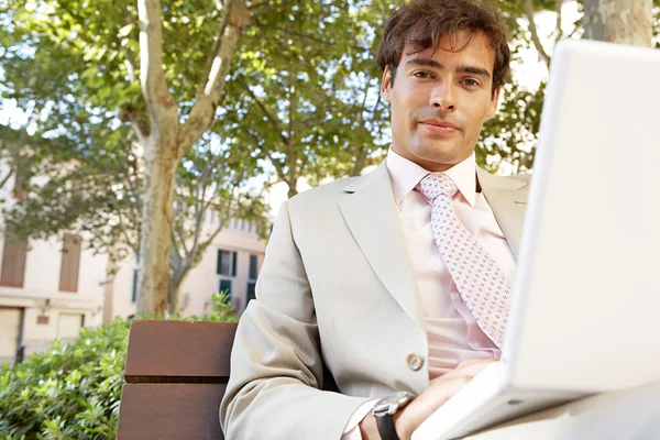 Professionele jongeman met behulp van een laptop pc zittend op een bank in een klassieke stadsplein. — Stockfoto