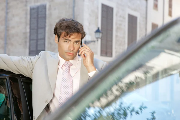 使用一部手机打个电话站立时由一些汽车在城市中的商人. — 图库照片