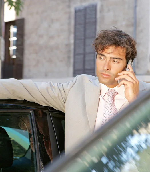 Businessman using a cell phone to make a phone call while standing by some cars in the city. — Stock Photo, Image