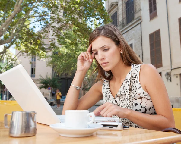 Femme d'affaires utilisant un ordinateur portable et regardant inquiet tandis que assis à une terrasse de café dans une ville classique — Photo