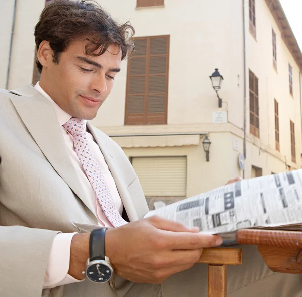 Homem de negócios atencioso lendo a seção classificada de um jornal enquanto sentado em um terraço de café — Fotografia de Stock