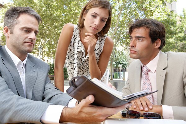 Three business having a meeting while sitting at a coffee shop terrace outdoors.