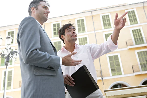 Two businessmen standing and talking near a classic building in a European city. — Stock Photo, Image