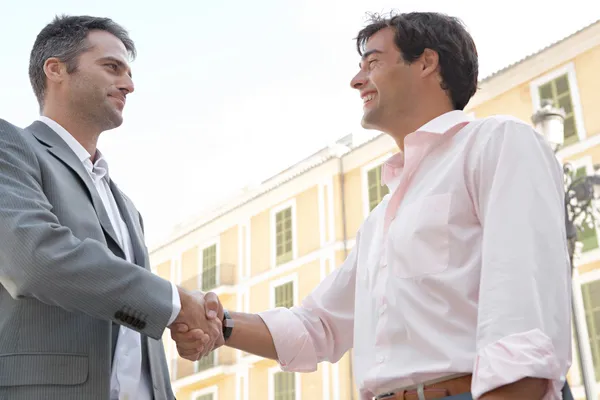 Два бизнесмена пожимают руки, стоя перед классическим европейским зданием — стоковое фото