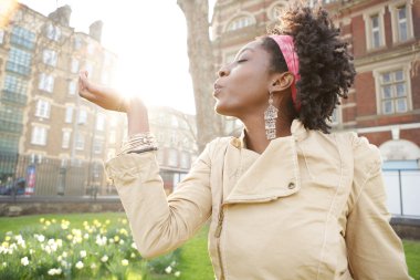 Beautiful young black woman holding the sun in her hand at sunset while visiting London city. clipart