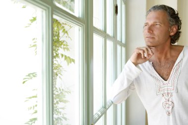 Olgun adam evde, büyük bir pencereden dışarı bakarak düşünceli.