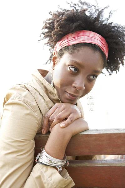Jovem mulher americana africana atraente sendo pensativo enquanto sentado em um banco em um parque da cidade . — Fotografia de Stock