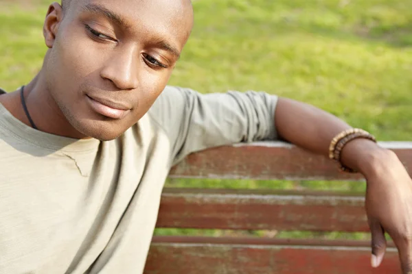 Ελκυστική αφρικανική αμερικανική άνθρωπος που είναι στοχαστικός, ενώ κάθεται σε ένα παγκάκι σε ένα πάρκο. — Φωτογραφία Αρχείου