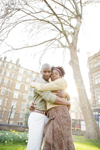 Young black couple hugging in a park at sunset, while visiting London city.