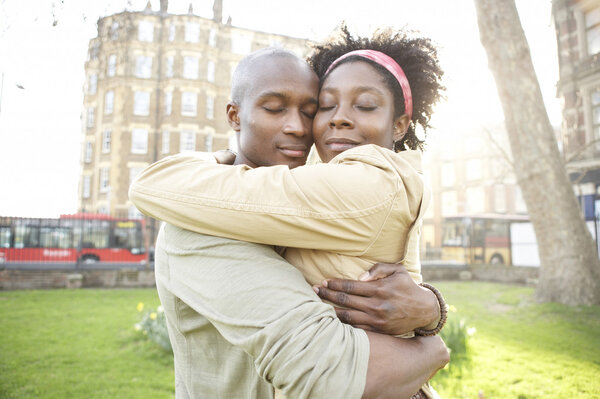Young couple hugging each other in the city at sunset, smiling.
