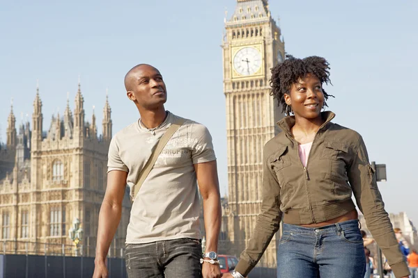 Aantrekkelijke zwarte toeristische paar hand in hand en wandelen langs de big ben tijdens een bezoek aan Londen stad op vakantie. — Stockfoto