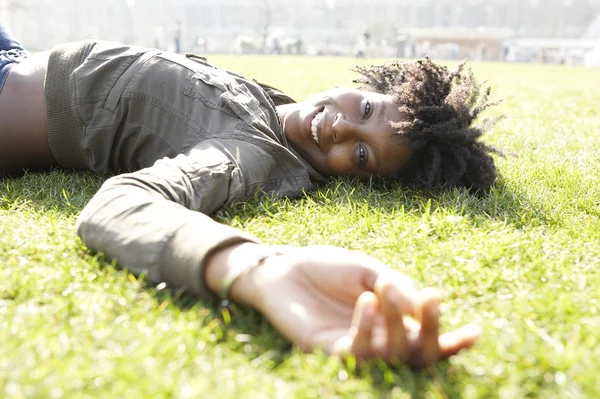 Unga afroamerikanska kvinnan fastställande på grönt gräs i staden, på en solig dag. — Stockfoto