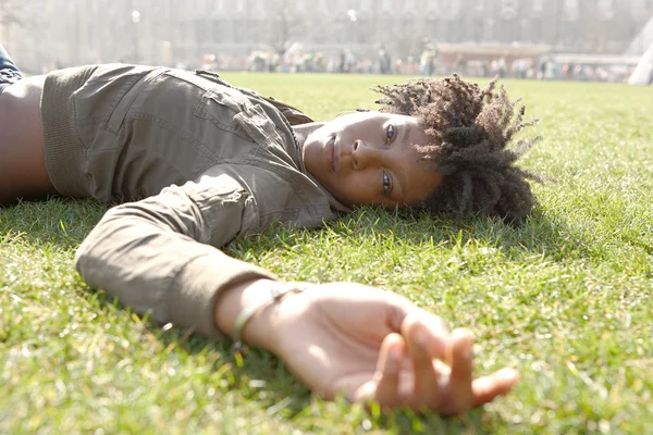 Привлекательная молодая черная женщина, лежащая на зеленой траве в Лондоне в солнечный день — стоковое фото