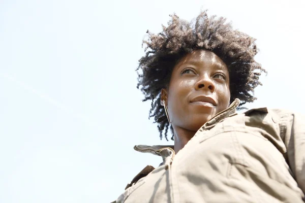 Portret van een aantrekkelijke jonge zwarte vrouw tegen een blauwe hemel, close-up glimlachen. — Stockfoto