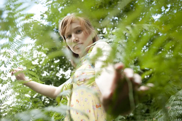 Adolescente regardant à travers le feuillage de la forêt, regardant dans la caméra . — Photo