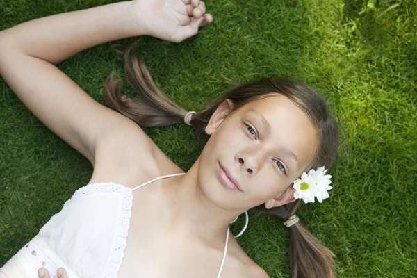 Teenage girl laying down on green grass, looking at camera. — Stock Photo, Image