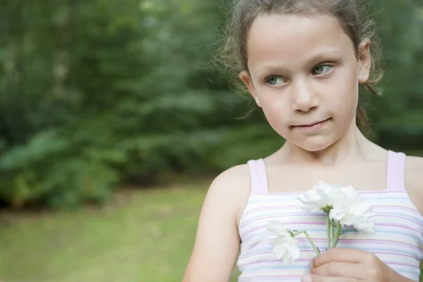 Mladá dívka drží květiny v lese. — Stock fotografie