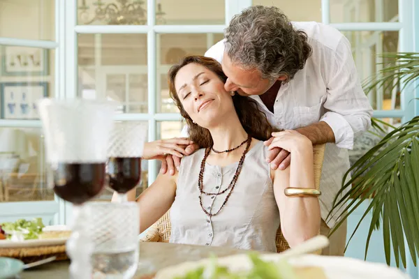 Hombre maduro besando a la mujer mientras está sentado en la mesa de almuerzo saludable, al aire libre . — Foto de Stock