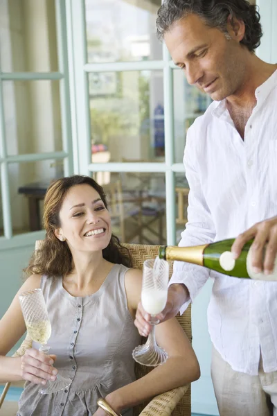 Зрілий чоловік вливає шампанське у флейтові окуляри з партнером вдома . — стокове фото