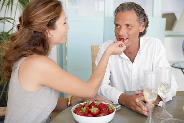 Mujer alimentando a hombre fresas mientras está sentado en una mesa al aire libre en casa . — Foto de Stock