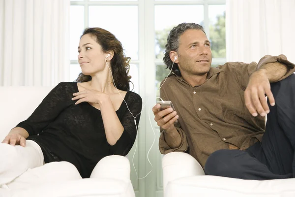 Ältere Paare teilen sich Kopfhörer, während sie im heimischen Wohnzimmer Musik mit einem mp4 hören. — Stockfoto