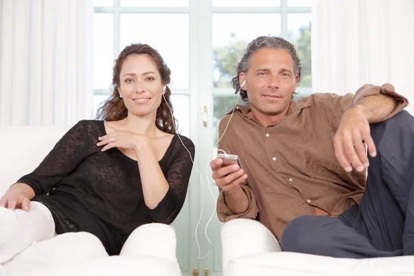 Mature couple sharing headphones while listening to music at home. — Stock Photo, Image