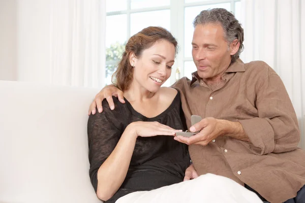 Зрелый мужчина предлагает обручальное кольцо зрелой женщине, сидя дома на белом диване . — стоковое фото