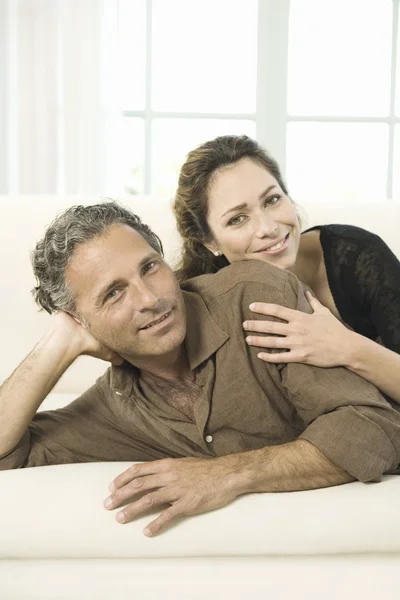 Porträtt av en äldre par fastställande på en vit soffa, ler mot kameran. — Stockfoto